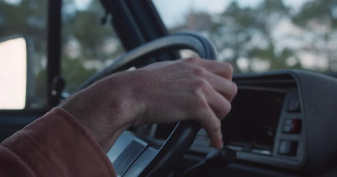 Details of a young man driving in his vintage van towards the cliffs and coastline of the Algarve to watch the upcoming sunset with blue sky in background and steering wheel in his hands, Portugal