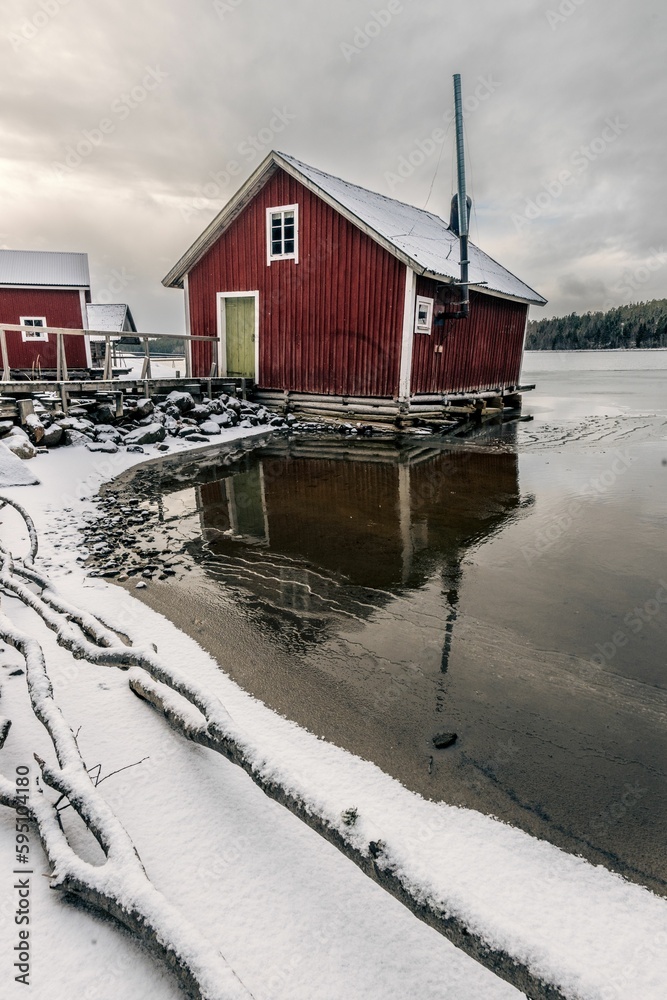 Sticker snowy shore of a pond with a rural red barn on a cloudy day