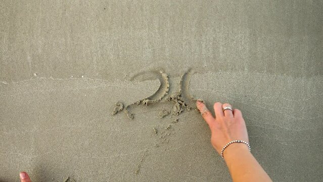 Young woman writing 2025 new year with finger on wet sea beach sand.