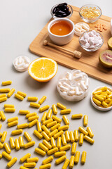 Natural vitamins from fruits and honey and vitamin pills, organic minerals in small bowls from above on wooden desk on light background. Orange, kiwi and honey as sources of natural vitamins.