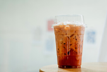 Thai tea, iced milk tea with milk in plastic cup on wooden table in coffee shop.