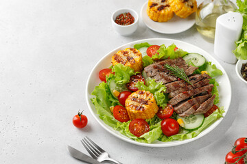 Roast beef salad on white plate and grey background. Salad, meal with meat steak, grilled corn and beef meat with vegetable. Diet dinner concept.