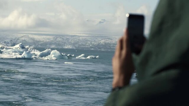 Tourist taking photo with smartphone of  iceberg on Iceland. Man taking picture with smart phone camera on travel visiting tourist attractions and landmarks in Icelandic nature 