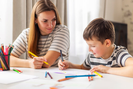 Mother and child drawing with pencils sitting at the desk at home