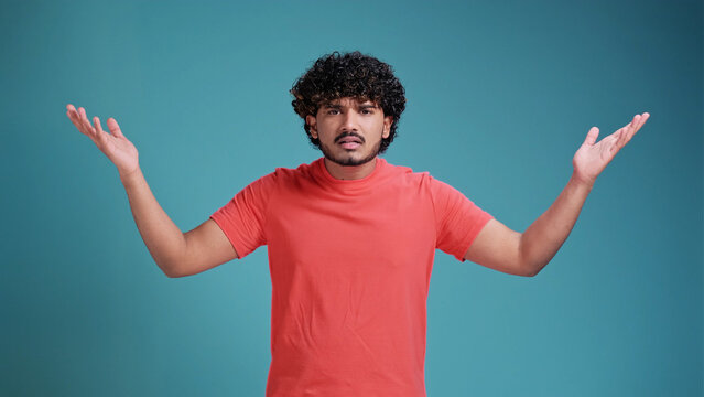 I don't know, who cares. Portrait of confused clueless brunette latin spanish man shrugging shoulders, making no idea gesture, whatever. isolated on a blue studio background