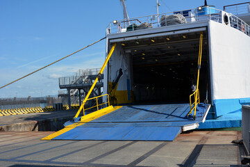 A large ferry has docked in the port and is waiting for passengers and cars with an open ramp