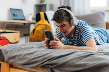 Caucasian adolescent boy is using a mobile phone while laying on the bed