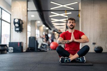 Fototapeta na wymiar Athletic man in sports clothes with hands clasped practicing Yoga meditation, sitting on exercise mat at health club.