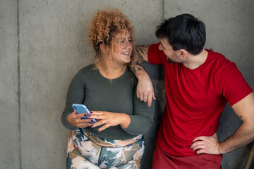 Active couple looking at each other with smile, standing together against the wall in gym, taking a...