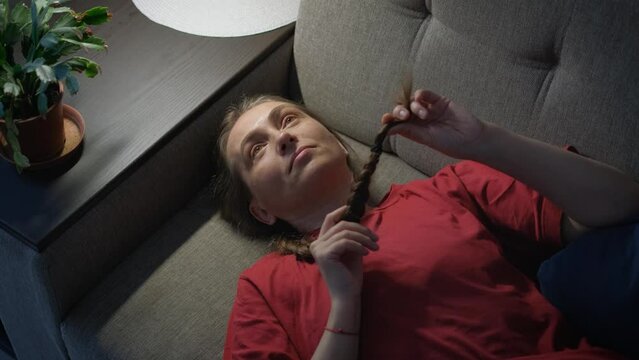 A woman in prostration lies on a sofa and twists a braided braid of hair in her hands