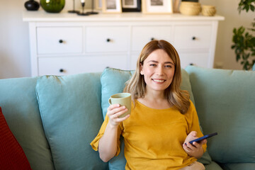 Woman using smartphone while drinking coffee at her home in the morning