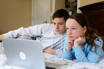 Overjoyed Kids sister brother laughing spend weekend free time together at home on couch bed eating popcorn. teen children watching video cartoon use remote control on laptop have fun