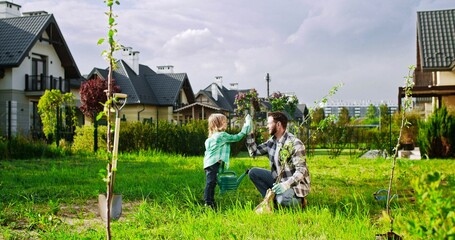Happy cheerful father and cute small son working in garden together and giving high five to each...