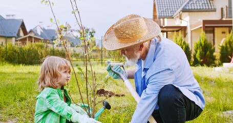 Little cute Caucasian boy helping his grandfather in planting trees in garden on sunny day. Small boy helping to grandpa in orchard. At village. Close up. - Powered by Adobe