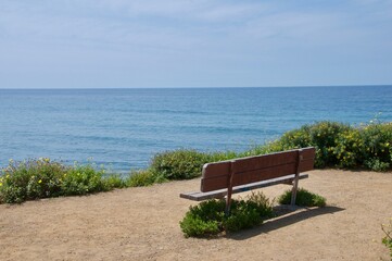Solitary bench on cliff overlooking Pacific Ocean Malibu California blue skies space