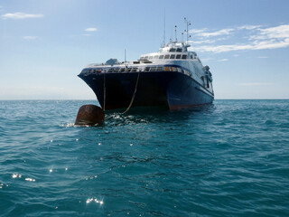 A large ship is moored to a buoy at sea on a calm turquoise sea. Tourist landscape