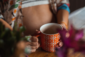 Young boho chic pregnant woman drinking a cup of coffee or tea.