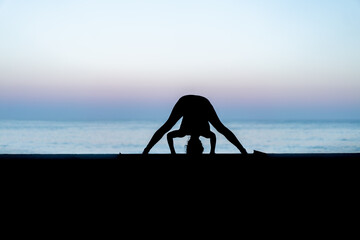 Silhouette de femme faisant du yoga devant la mer au coucher de soleil, posture Prasarita...