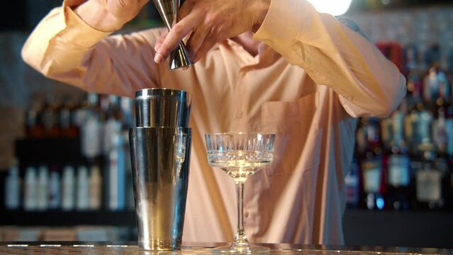 Professional bartender masterly creating a cocktail in modern bar. Experienced barman adding syrip into shaker using jigger - food and drink