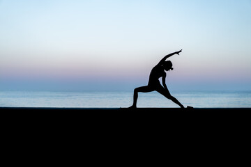 Silhouette de femme faisant du yoga devant la mer au coucher de soleil, posture Viparita...