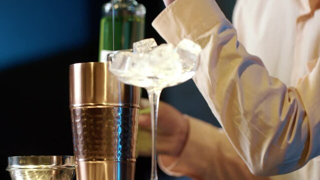 Professional bartender masterly creating a cocktail in modern bar. Experienced barman adding syrip into shaker using jigger - food and drink