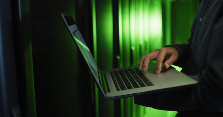 Composition of green light over african american businessman using laptop in server room