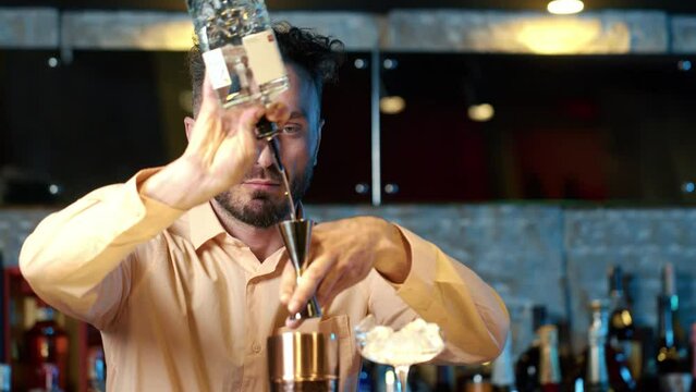 Professional bartender masterly creating a cocktail in modern bar. Experienced barman adding syrip into shaker using jigger - food and drink