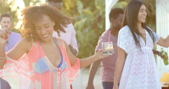 Happy diverse group of friends dancing holding cocktails at beach