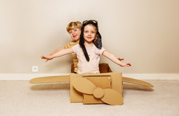 Children sit in cardboard plane wear hats and glasses wave hands