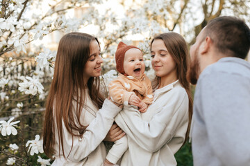 A little baby in the arms of twin sisters was delighted when she saw her father in the blooming garden. Lifestyle. Family concept. Father and Daughter. 