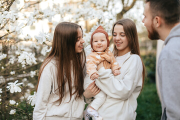 A little baby in the arms of twin sisters was delighted when she saw her father in the blooming garden. Lifestyle. Family concept. Father and Daughter. 