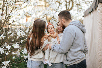Fototapeta premium A little baby in the arms of twin sisters was delighted when she saw her father in the blooming garden. Lifestyle. Family concept. Father and Daughter. 