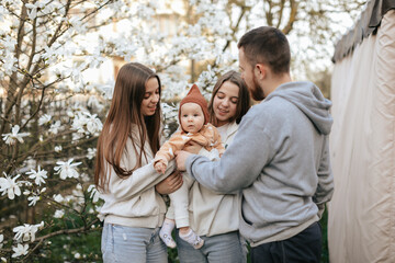 A little baby in the arms of twin sisters was delighted when she saw her father in the blooming garden. Lifestyle. Family concept. Father and Daughter. 
