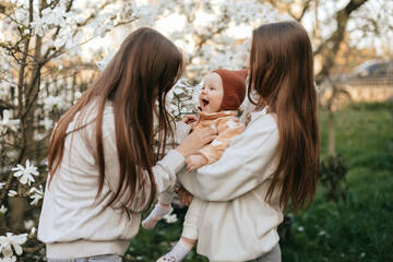 Twin girls are playing with their younger sister in a blooming garden. Family concept. Lifestyle family. 