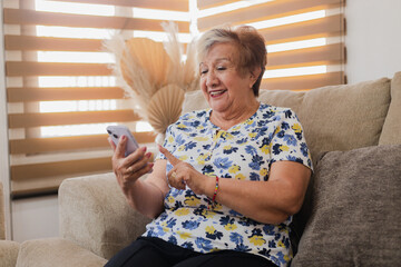 60-year-old woman with a smartphone in her hands-grandmother smiling while she is talking on a...