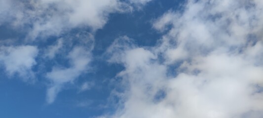 Bright sky above. Spring sunny day, white clouds slowly float in the blue sky. They hang at a low height and they have different shapes and sizes. The clouds are clear and light in spring.