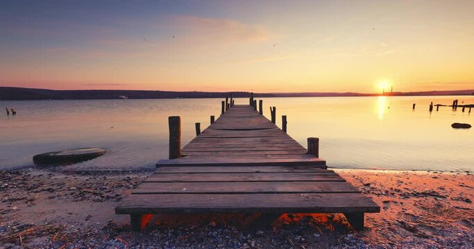 Sea lake sunset over old wooden jetty pier on the shore, relaxing nature landscape, 4k video