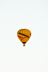 Vertical image of super telephoto shot of hot air balloon isolated against white sky background in early morning flight.