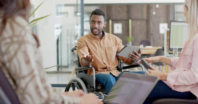 Disabled diverse businessman in wheelchair using tablet with colleagues and talking in slow motion