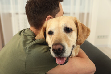 Man hugging his cute Labrador Retriever at home, back view
