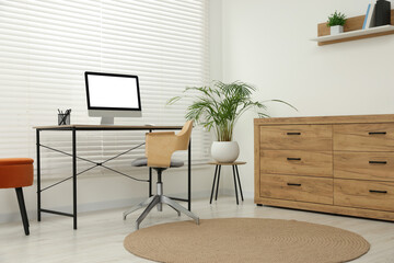 Stylish office interior with comfortable chair, desk, computer and houseplant