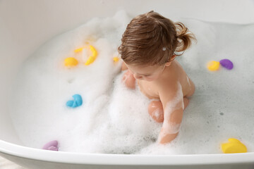 Cute little girl taking bubble bath with toys indoors