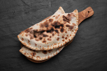 Wooden board with delicious calzones on black table, top view