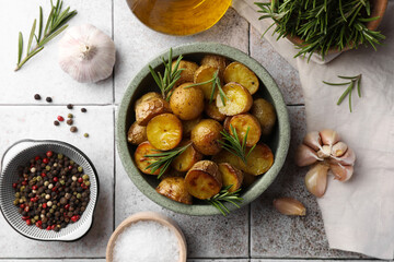 Flat lay composition with tasty baked potato and aromatic rosemary on light tiled table