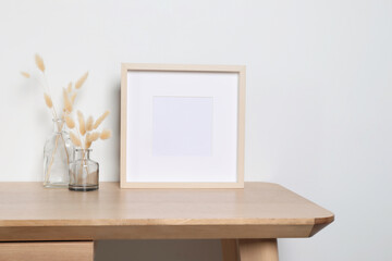 Empty photo frame and vases with dry decorative spikes on wooden table. Mockup for design
