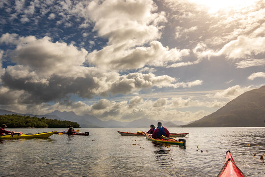 sea kayakers on the water beneath dramatic white clouds in the chonos archipelago, patagonia, chile
