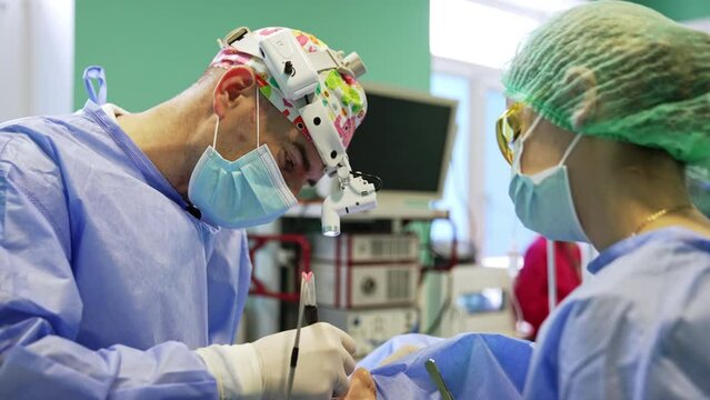 Concentrated surgeon wearing headlight applies electric device. Doctor uses metal instruments at eyelid surgery.