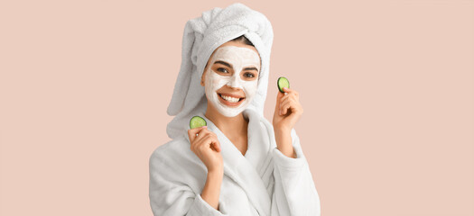 Beautiful young woman with cucumber slices and facial mask on beige background