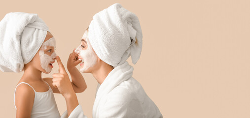 Portrait of mother and little daughter with facial masks on beige background