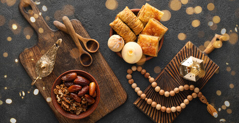 Tasty Eastern sweets with tasbih and Arabic lamps on dark background
